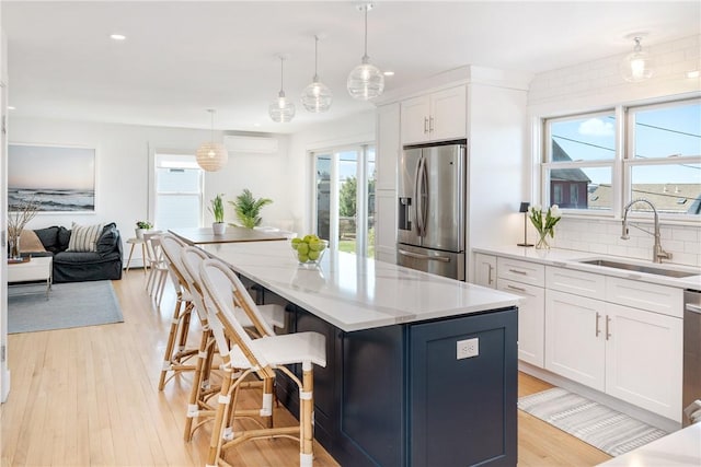 kitchen with a wall mounted air conditioner, stainless steel appliances, a sink, a center island, and white cabinetry