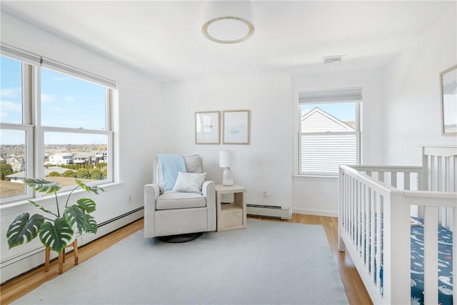 bedroom featuring baseboard heating, multiple windows, wood finished floors, and visible vents