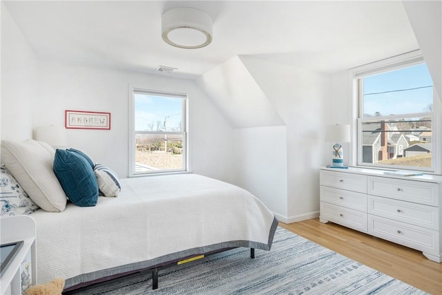 bedroom featuring visible vents, light wood-style flooring, baseboards, and vaulted ceiling
