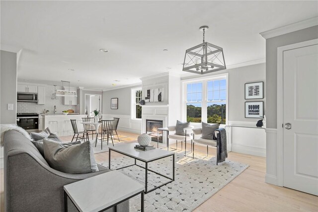 0 Greenwich Blvd Unit 110, East Greenwich, RI 02818 - living room featuring ornamental molding, a chandelier, a glass covered fireplace, light wood-style flooring, and a wainscoted wall