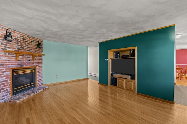 unfurnished living room with hardwood / wood-style floors, baseboards, a brick fireplace, and a textured ceiling