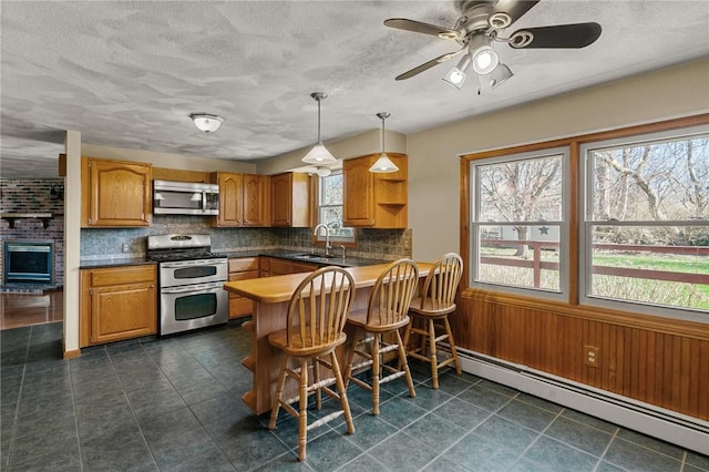 kitchen with appliances with stainless steel finishes, a baseboard heating unit, a sink, brown cabinets, and backsplash
