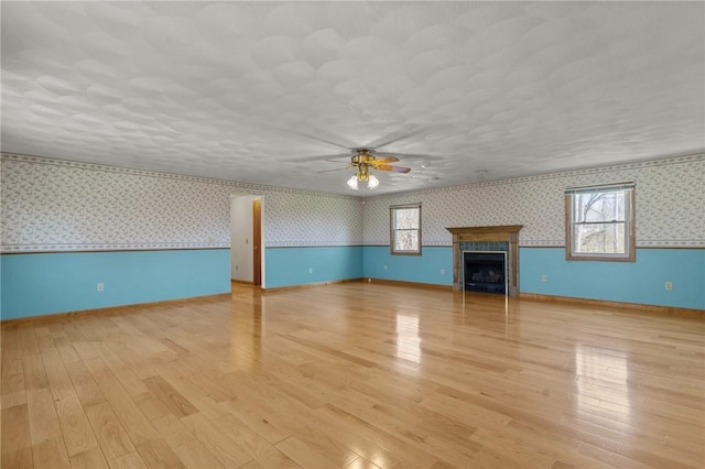unfurnished living room with plenty of natural light, light wood-style floors, wallpapered walls, and a ceiling fan