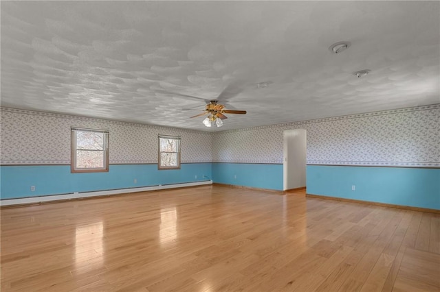 spare room featuring a baseboard heating unit, wallpapered walls, a ceiling fan, and wood finished floors