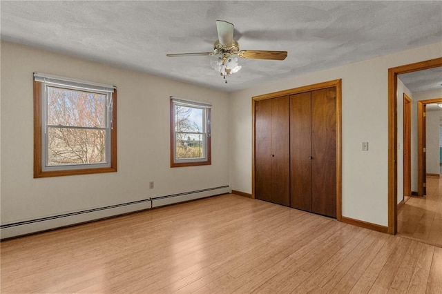 unfurnished bedroom with baseboard heating, a closet, light wood-type flooring, baseboards, and a ceiling fan