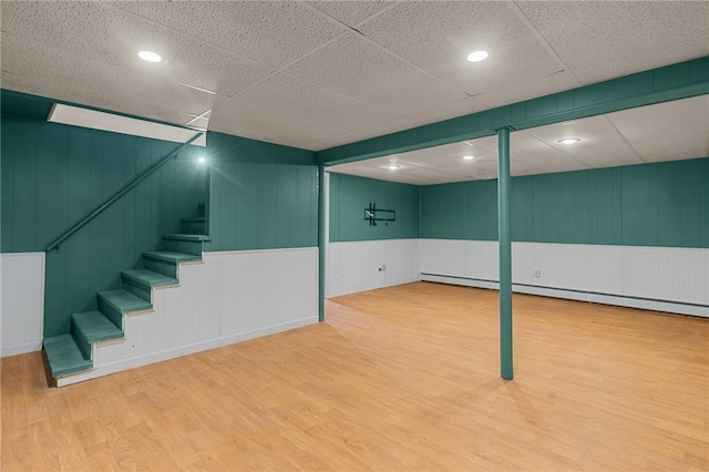 finished basement with a decorative wall, wainscoting, wood finished floors, and stairs