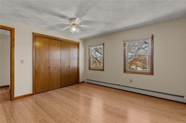 unfurnished bedroom with baseboard heating, a closet, baseboards, ceiling fan, and light wood finished floors