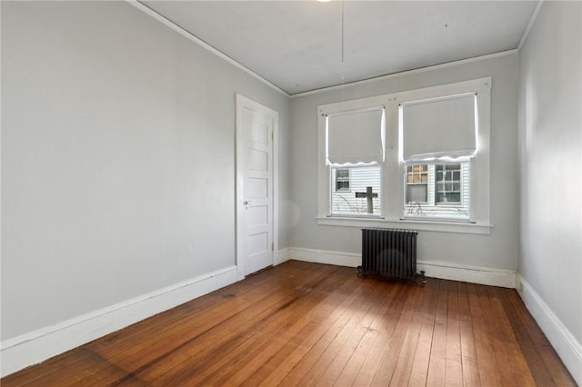 spare room featuring wood-type flooring, radiator heating unit, crown molding, and baseboards