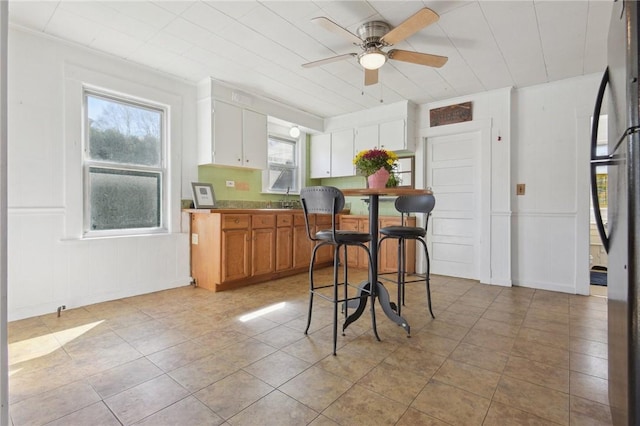 kitchen featuring freestanding refrigerator, a decorative wall, ceiling fan, and light tile patterned floors
