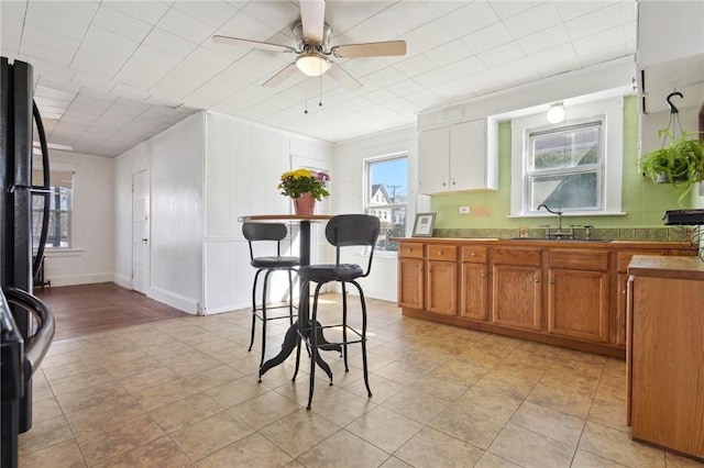 kitchen featuring a sink, brown cabinetry, light tile patterned flooring, ceiling fan, and freestanding refrigerator
