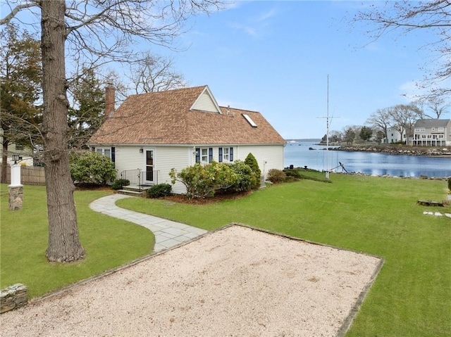 back of house with a shingled roof, a chimney, a lawn, and a water view