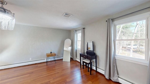 living area featuring a baseboard heating unit, wood finished floors, and a healthy amount of sunlight