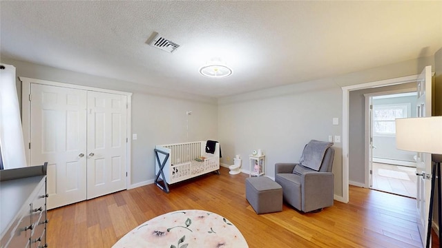 bedroom featuring visible vents, baseboards, a closet, a baseboard radiator, and light wood-style flooring
