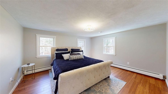 bedroom with multiple windows, wood finished floors, and baseboard heating