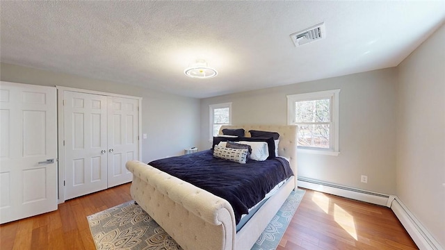 bedroom featuring visible vents, baseboards, baseboard heating, and wood finished floors
