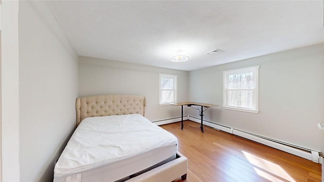 bedroom with a baseboard radiator, multiple windows, and wood finished floors