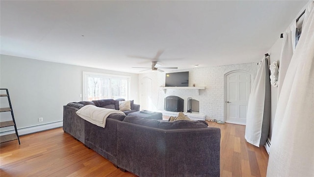 living area with a brick fireplace, ceiling fan, a baseboard radiator, and wood finished floors