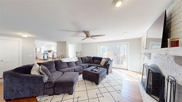living area with light wood-type flooring, baseboards, a ceiling fan, and a brick fireplace