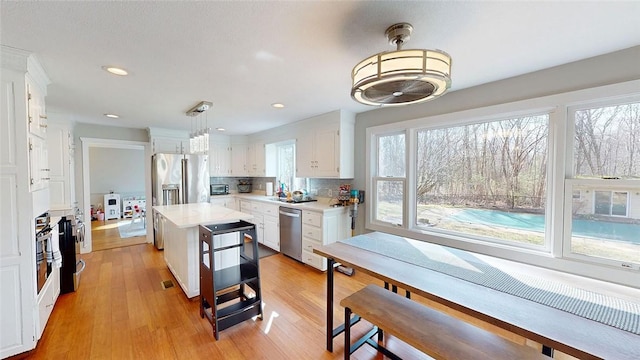 kitchen featuring tasteful backsplash, light countertops, appliances with stainless steel finishes, white cabinetry, and light wood finished floors