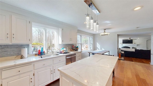 kitchen with white cabinetry, a kitchen island, decorative backsplash, dishwasher, and a sink