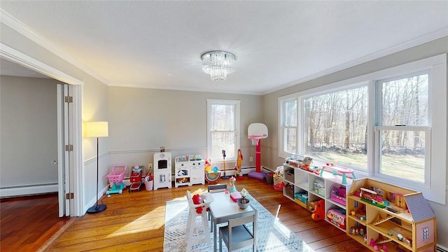 playroom featuring a notable chandelier, baseboards, a baseboard heating unit, crown molding, and wood finished floors