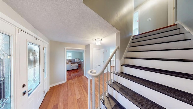 entryway featuring stairway, light wood finished floors, a textured ceiling, and baseboards