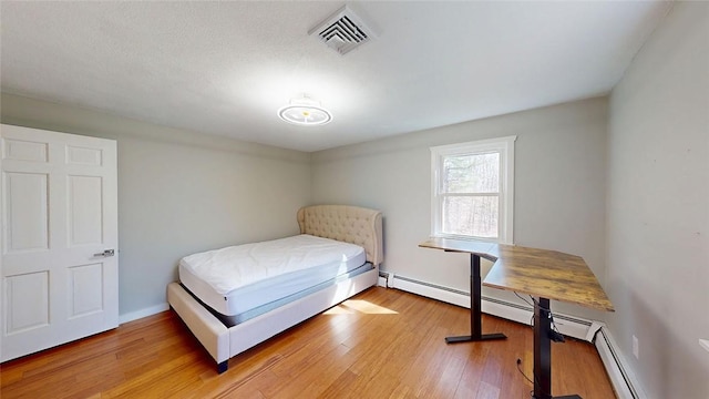bedroom featuring visible vents, baseboards, light wood-type flooring, and baseboard heating