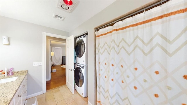 laundry room featuring baseboards, stacked washer and clothes dryer, light tile patterned floors, visible vents, and laundry area
