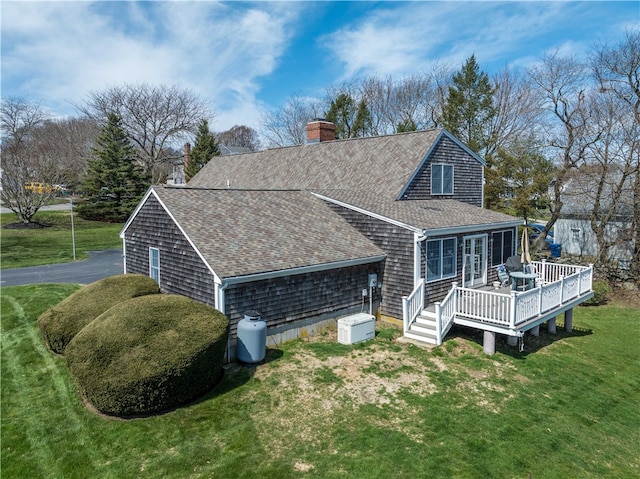 view of home's exterior with a shingled roof, a deck, a lawn, and a chimney