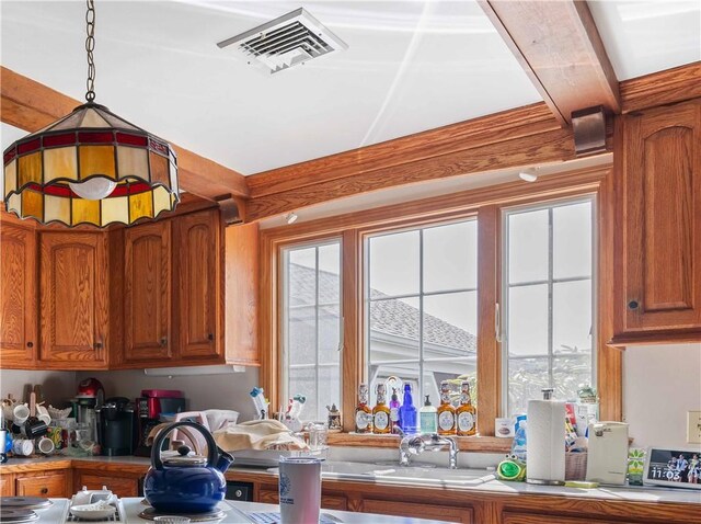 kitchen featuring visible vents, decorative light fixtures, a sink, light countertops, and brown cabinets