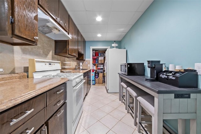 174 Windmill Dr, South Kingstown, RI 02879 - kitchen featuring light tile patterned floors, dark brown cabinetry, under cabinet range hood, and white appliances