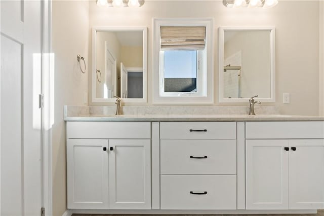 bathroom featuring a shower stall, double vanity, and a sink