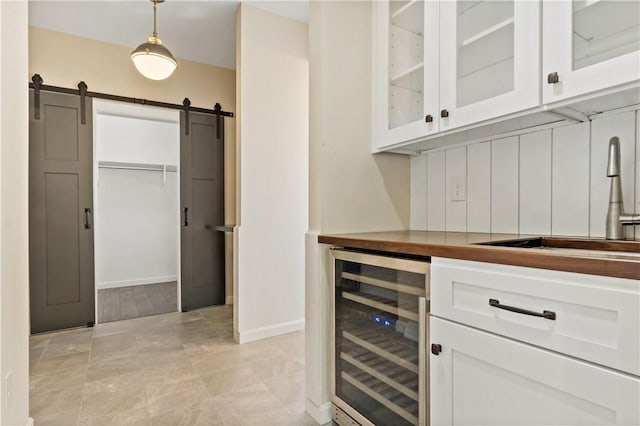 bar with baseboards, a barn door, a sink, pendant lighting, and beverage cooler
