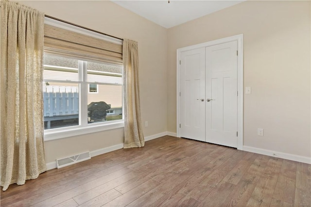unfurnished bedroom with a closet, visible vents, baseboards, and wood finished floors