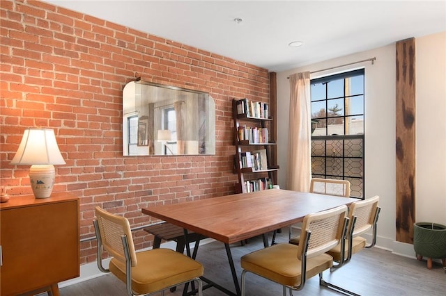 dining room featuring brick wall, wood finished floors, and baseboards
