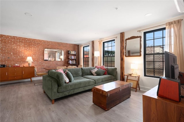 living room with brick wall, light wood finished floors, and baseboards