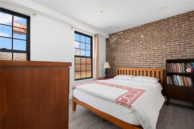 bedroom featuring brick wall and wood finished floors