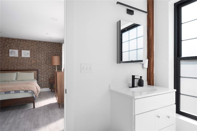 bedroom featuring brick wall, an accent wall, light wood-type flooring, and a sink