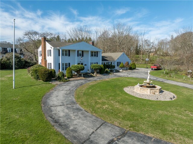 neoclassical / greek revival house featuring a chimney, curved driveway, and a front yard