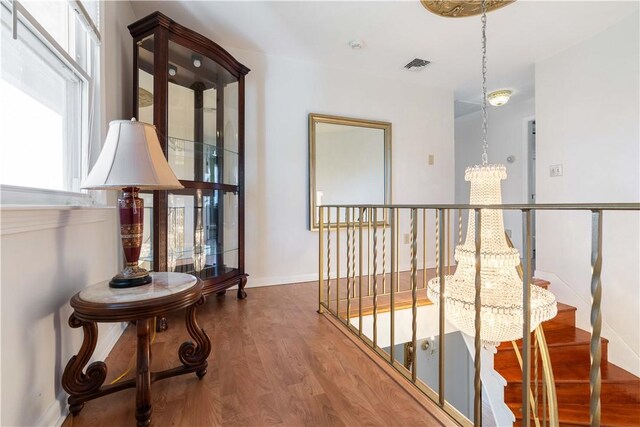 hall featuring wood finished floors, an inviting chandelier, stairway, baseboards, and visible vents