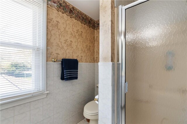 full bathroom with tile walls, a shower stall, toilet, a wainscoted wall, and wallpapered walls