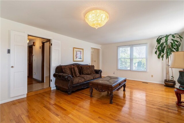 living area featuring an inviting chandelier, visible vents, light wood finished floors, and baseboards