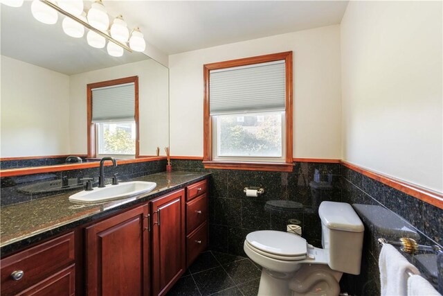 half bathroom featuring granite finish floor, toilet, tile walls, vanity, and wainscoting