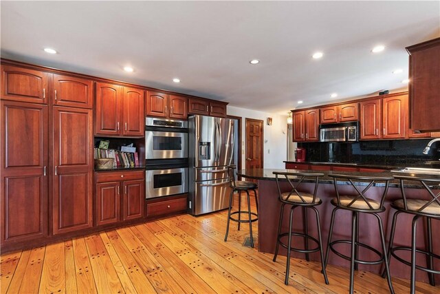 kitchen with recessed lighting, light wood-style floors, appliances with stainless steel finishes, a peninsula, and a kitchen breakfast bar