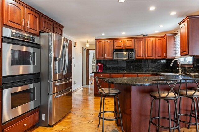 kitchen with a breakfast bar area, stainless steel appliances, decorative backsplash, and a sink