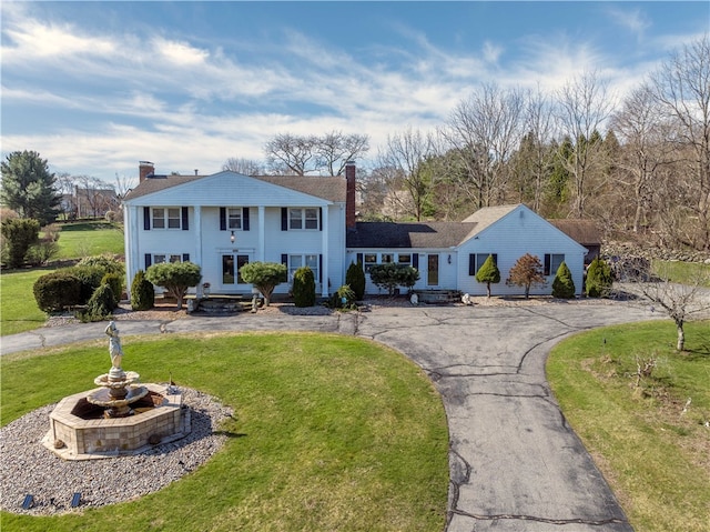 view of front of house featuring a chimney, a front lawn, and curved driveway