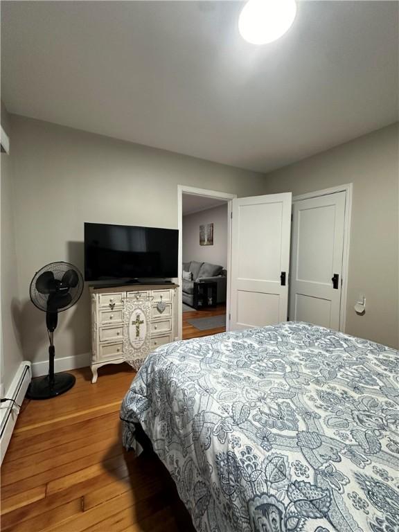 bedroom featuring wood finished floors, a baseboard heating unit, and baseboards