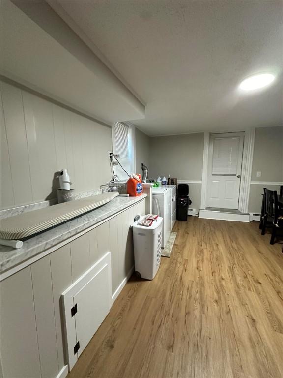 washroom with light wood-type flooring, washing machine and clothes dryer, cabinet space, and a baseboard radiator