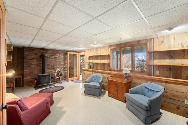 living area featuring tile patterned floors, a wood stove, wooden walls, and a paneled ceiling