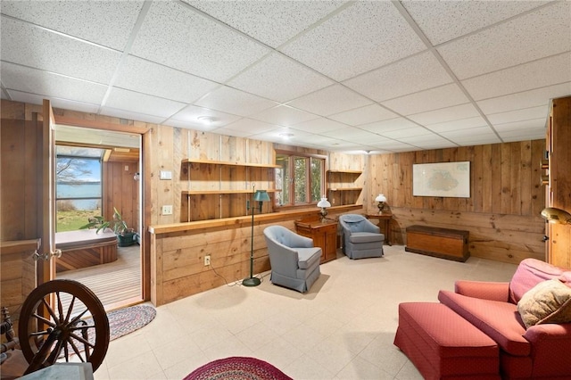 living area featuring wood walls, tile patterned floors, and a paneled ceiling